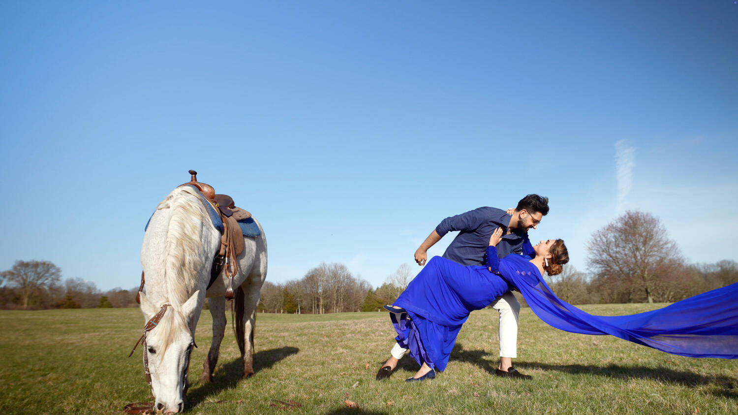 Bride and groom in a romantic dip pose beside a horse in an open field
