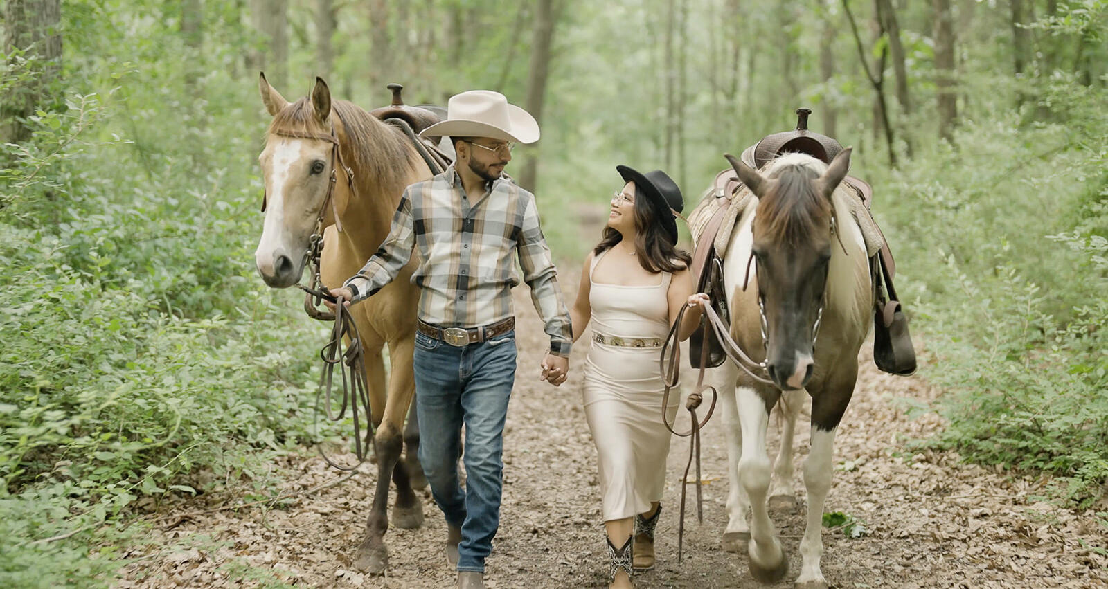 Bride and groom walking with two horses on a wooded trail
