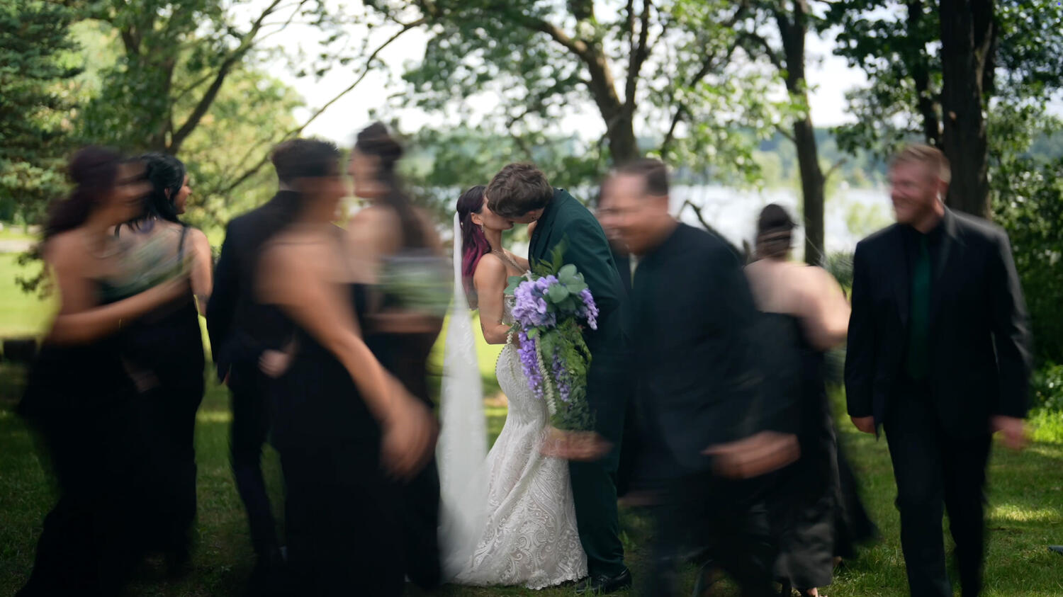 Bride and groom sharing a first kiss surrounded by their wedding party