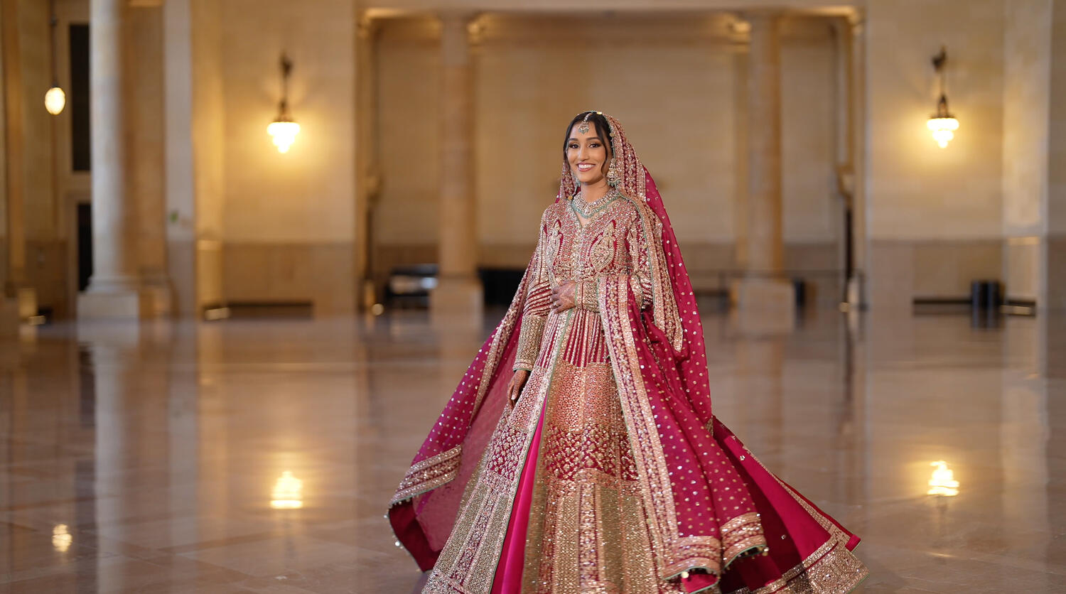 Bride in an ornate red and gold bridal lehenga standing in a grand hall